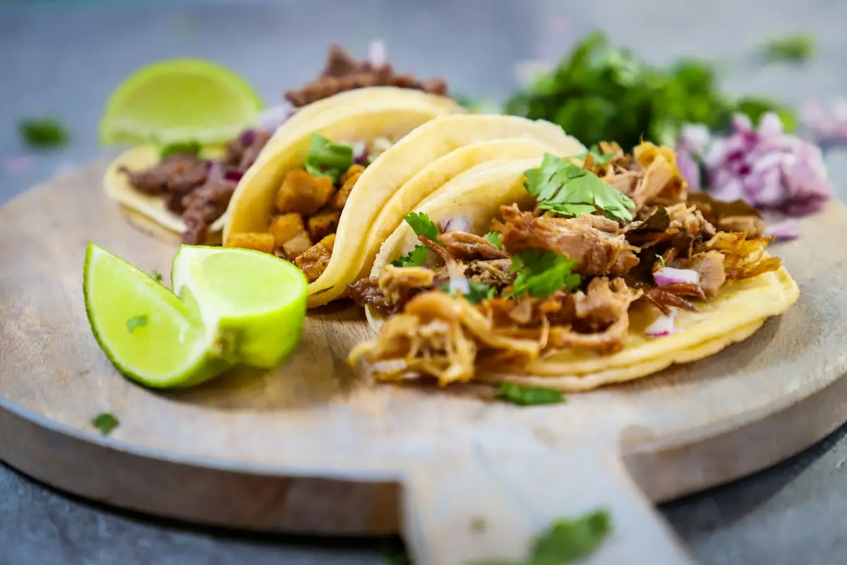 Tabla de madera con tres tacos y un limón